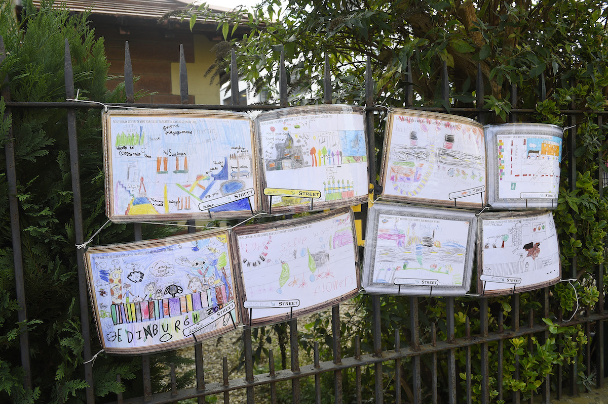 Paintings and drawings by primary school pupils of proposed road designs hanging on school railing