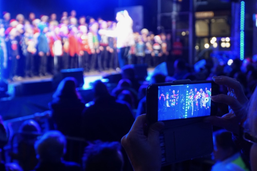 Smartphone in foreground with choir on stage