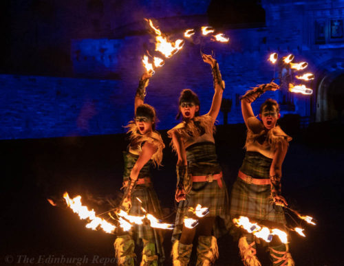 Three women with fiery hoops in front of blue castle