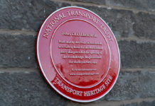 Red plaque on stone wall with white raised text National Transport Trust Transport Heritage Site