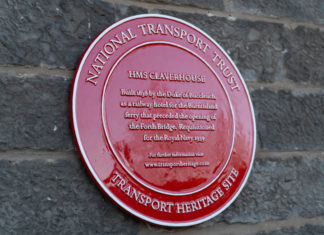 Red plaque on stone wall with white raised text National Transport Trust Transport Heritage Site