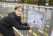 Primary schoolgirl showing her school street design hanging on a street railing