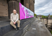 Photo of Derek Grainge a former pupil at the Royal High School sitting near the new-classical columns and beside a Hidden Door banner