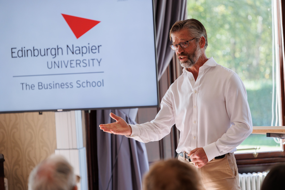 Professor in front of projector screen addressing audience