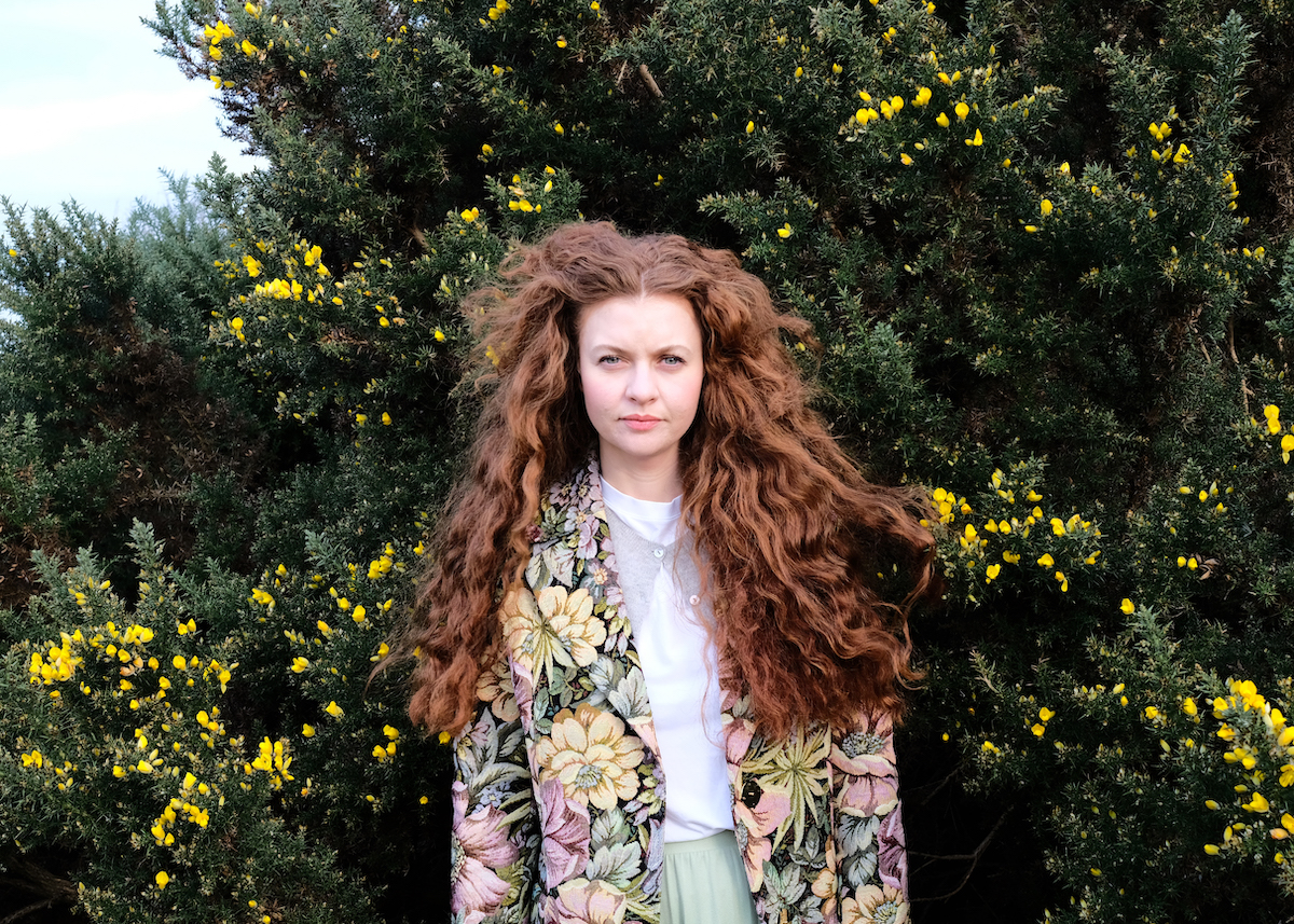 Close-up of Chloe Mullen - with stunning long red hair - in a green countryside setting