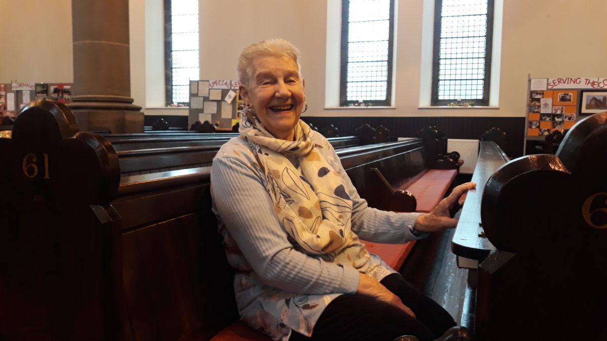 Elder, Helen O'Brien, smiling seated in a pew at St Michael's.